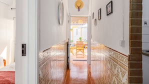 A hallway with patterned tiles, a door, a wall-mounted clock, and framed pictures.