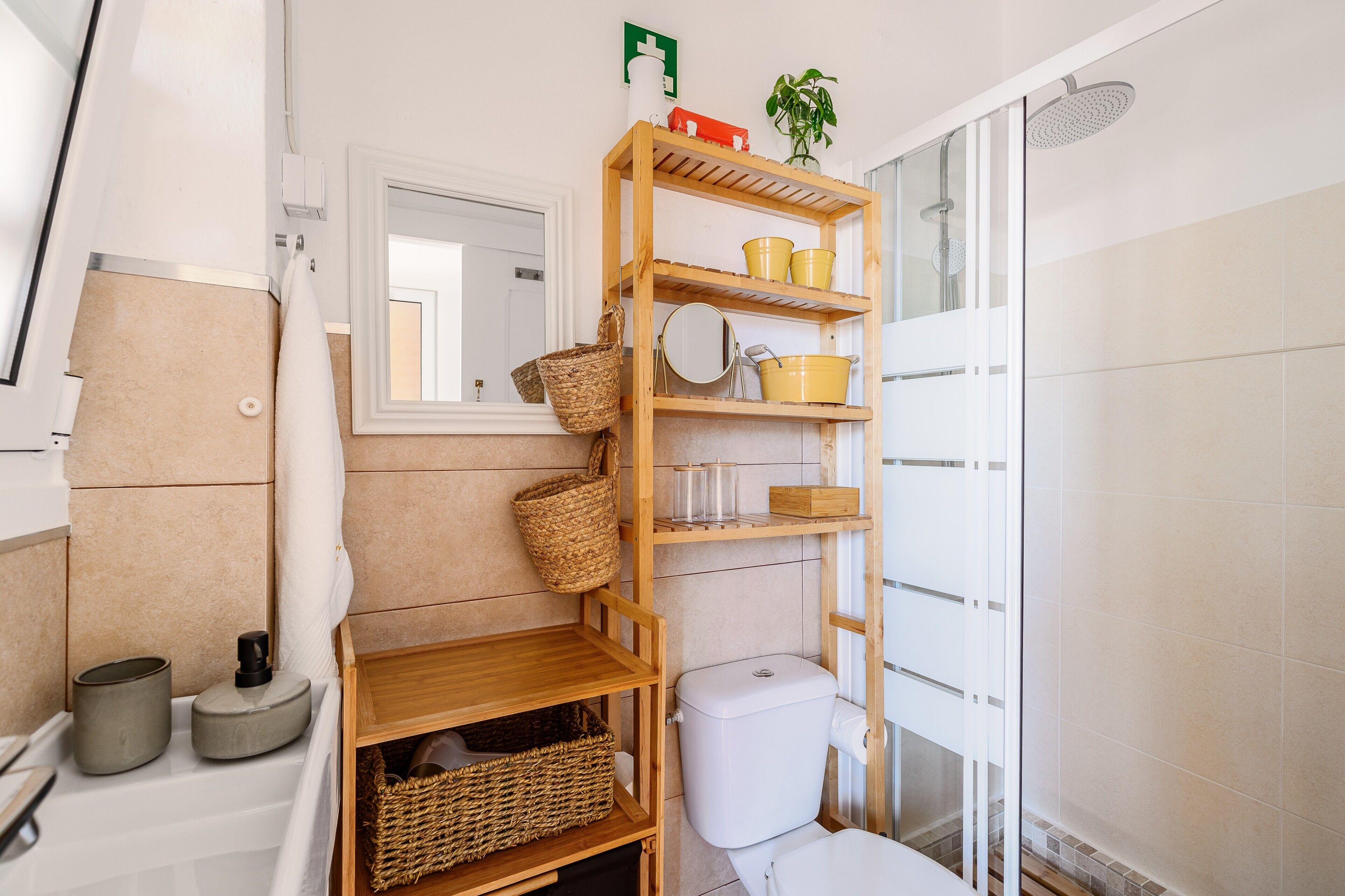 Ein Badezimmer mit Toilette, Dusche, Spiegel und einem Holzboden mit Körben und Pflegeprodukten.