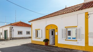 A two-story building with a yellow facade, a tiled roof, and a door with shutters.
