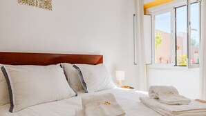 A neatly made bed with white linens and towels, a wooden headboard, and a window with a view of the outside.