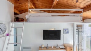 Une pièce avec un lit en mezzanine, un téléviseur fixé au mur, un globe terrestre et une petite statue posée sur une commode en bois.