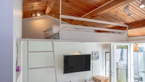 Une chambre avec un lit superposé, un téléviseur à écran plat, un plafond en bois et une porte-fenêtre coulissante donnant sur un espace extérieur.