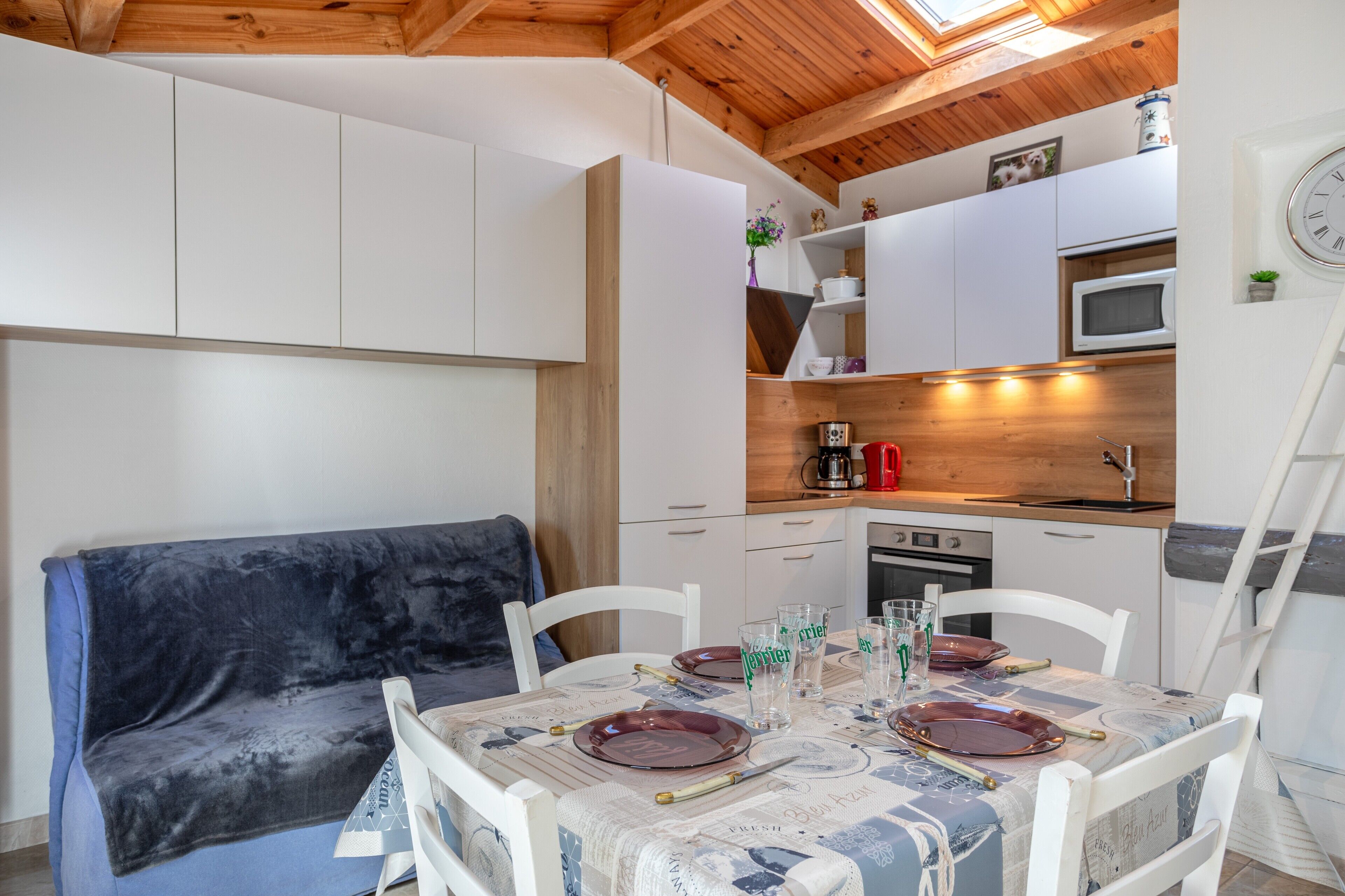 A compact kitchen with white cabinets, a microwave, and a sink. There is a dining table set with plates and glasses.