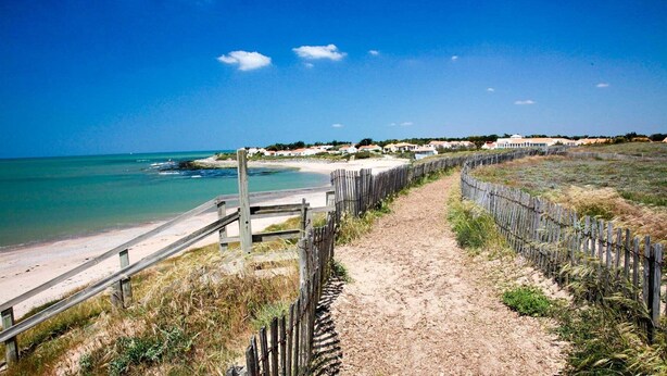 Un sentier qui longe la plage et mène à l’océan, avec une clôture en bois et une promenade en bois.