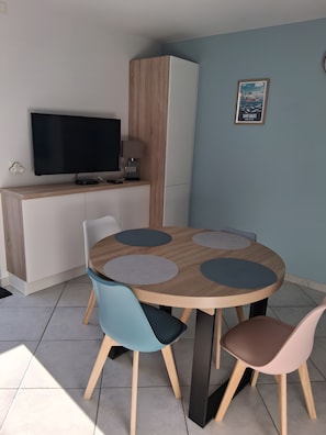A modern dining area with a round table, four chairs, a TV, and a cabinet.