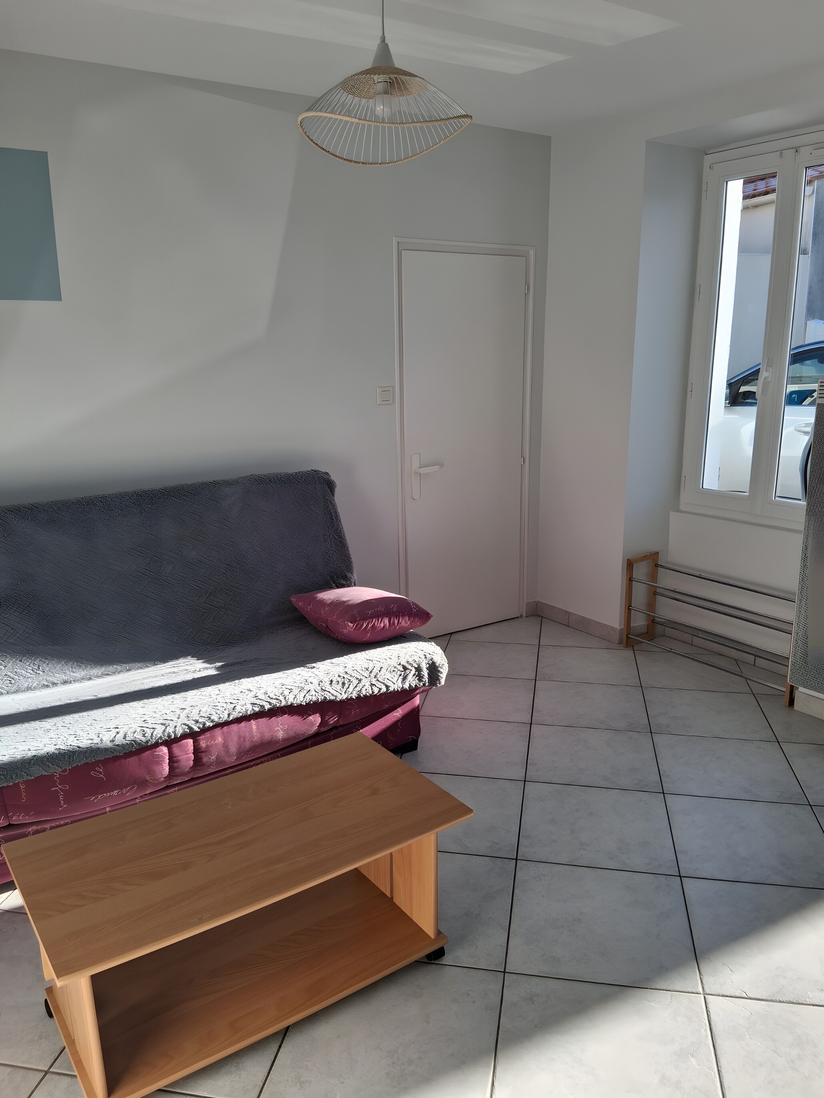 Une pièce comprenant un canapé, une table en bois, un luminaire suspendu, une porte et une fenêtre.