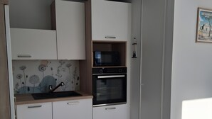Una cocina moderna con armarios blancos, microondas, horno y una lámpara colgante.