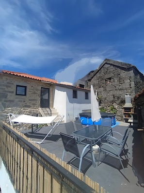 A patio with a table and chairs, a stone building with a red roof, and a wooden fence.
