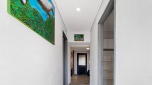 A hallway with a wooden floor, white walls, and a painting on the left.