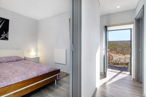 Une chambre à coucher avec un lit, une table de chevet et une vue sur un jardin, visible par une porte ouverte.