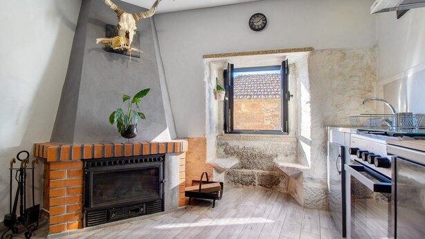 A kitchen with a brick fireplace, a stone wall, a window with a view, and a clock on the wall.