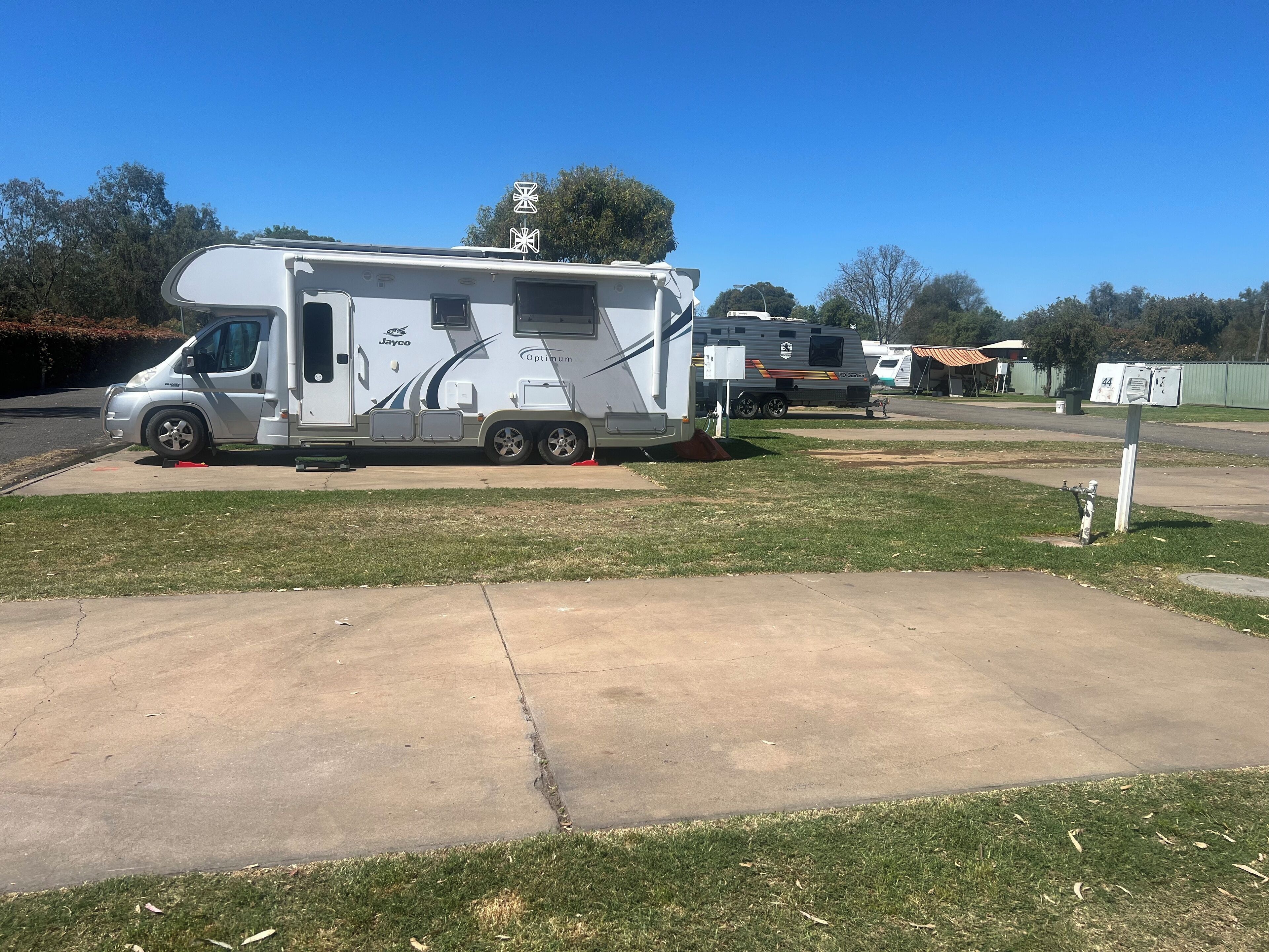 Una caravana Jayco Optimum DURA-TEK estacionada sobre un camino de hormigón con un césped delantero.