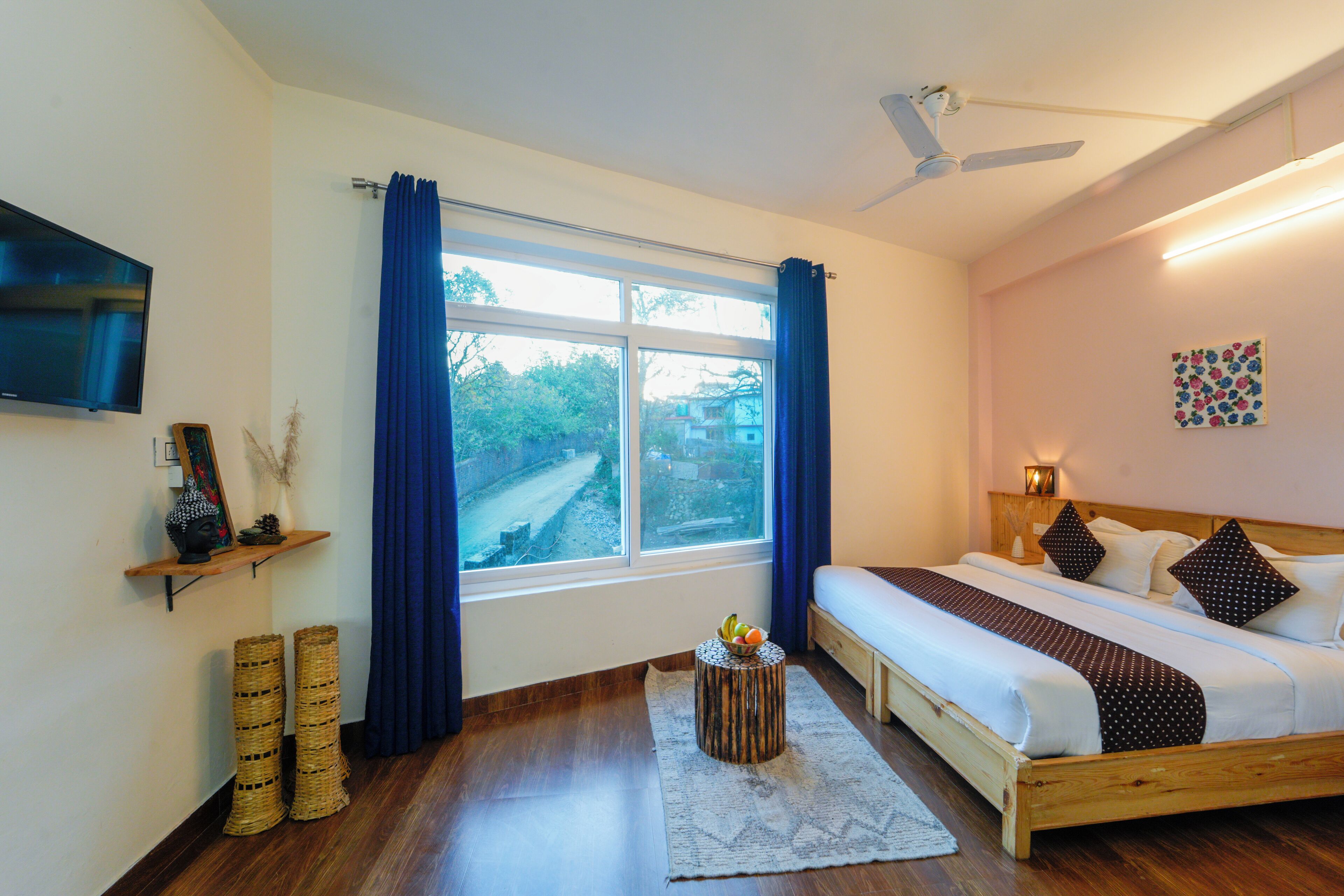 Une chambre à coucher avec un lit, un téléviseur fixé au mur, une fenêtre avec des rideaux et une table de chevet avec une lampe.