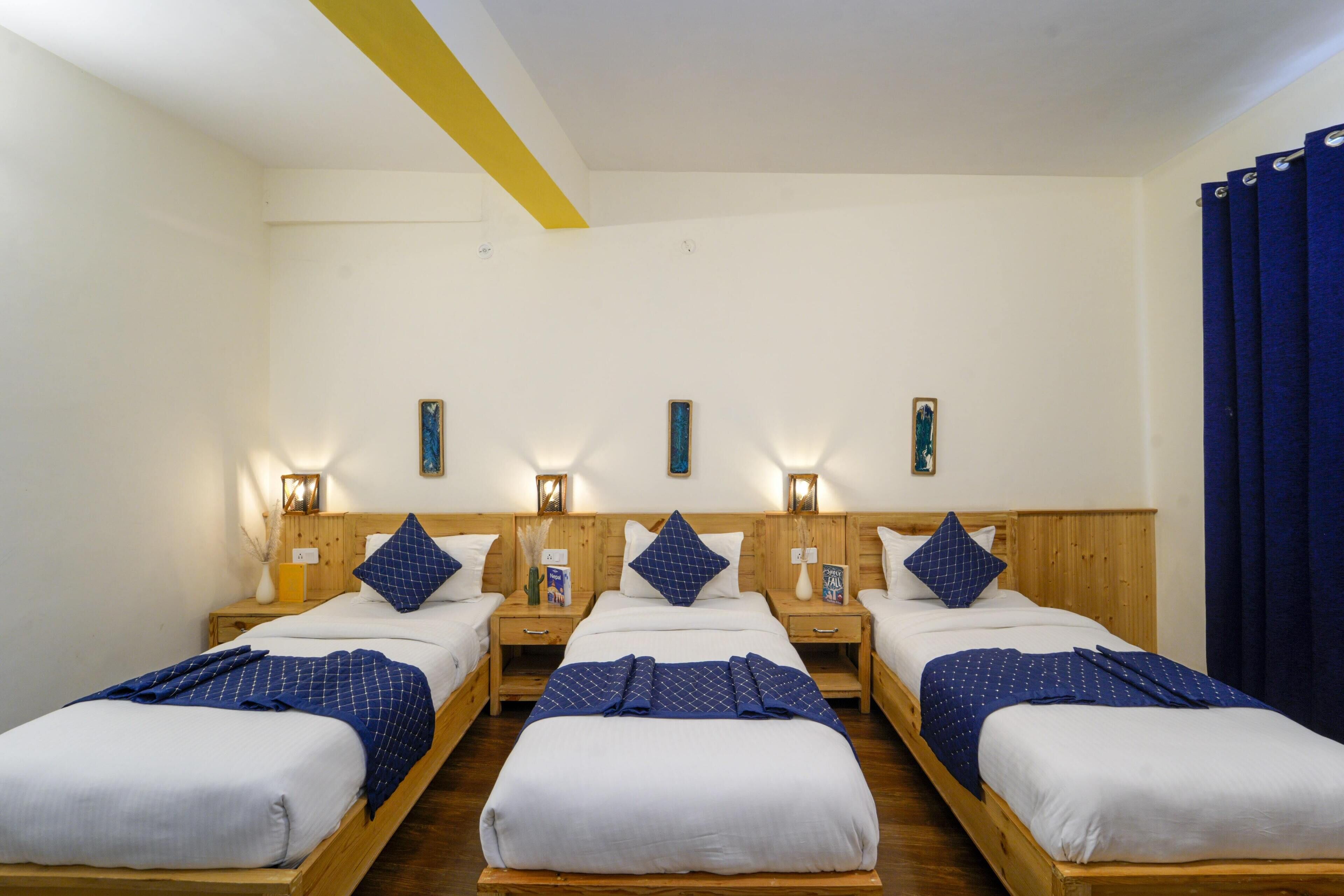 Una habitación de hotel con tres camas de madera, cada una con una colcha azul y blanca y almohadas a juego. Hay mesitas de noche con lámparas y pequeños adornos.
