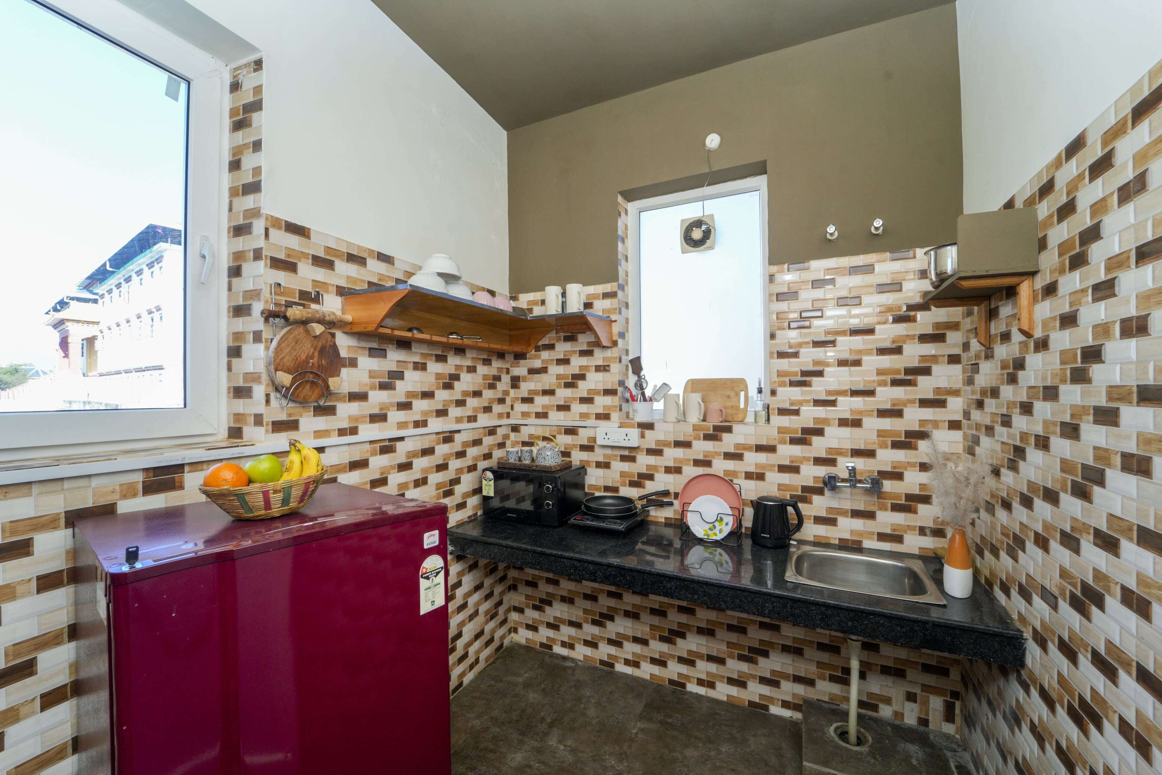 Una cocina compacta con salpicadero de azulejos, un refrigerador rojo, un lavamanos y una ventana con vistas a un edificio.