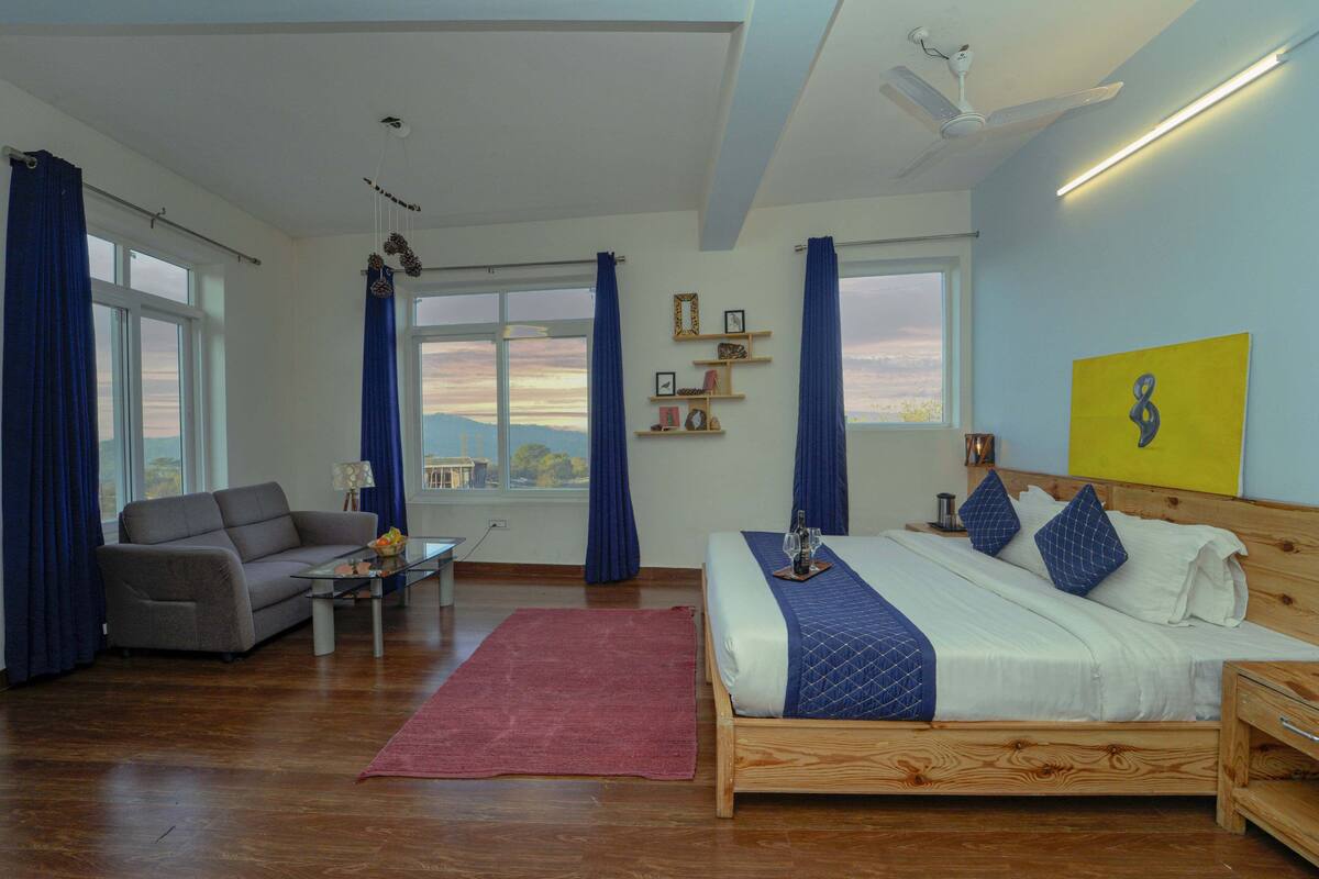 Ein Schlafzimmer mit einem hölzernen Bett, einem grauen Sofa, einem roten Teppich und Blick auf die Stadt durch das Fenster.