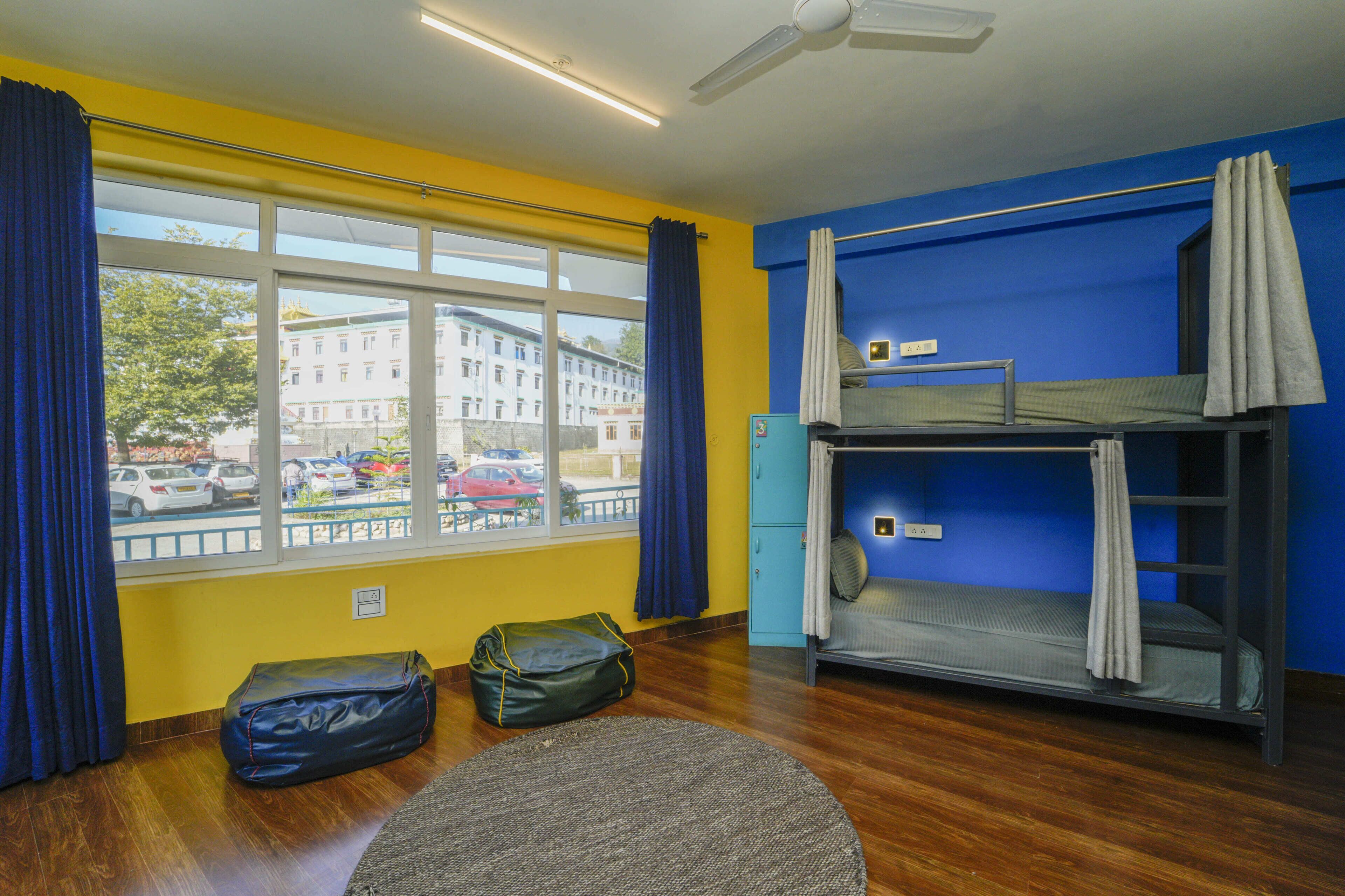 A room with a bunk bed, a window with curtains, a desk, and a bag on the floor.