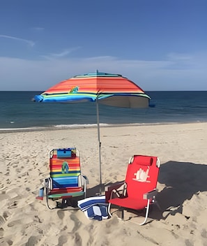 A beach with two beach chairs and a colorful umbrella.
