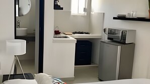 Un dormitorio con cama, escritorio, espejo, microondas y una planta en maceta.