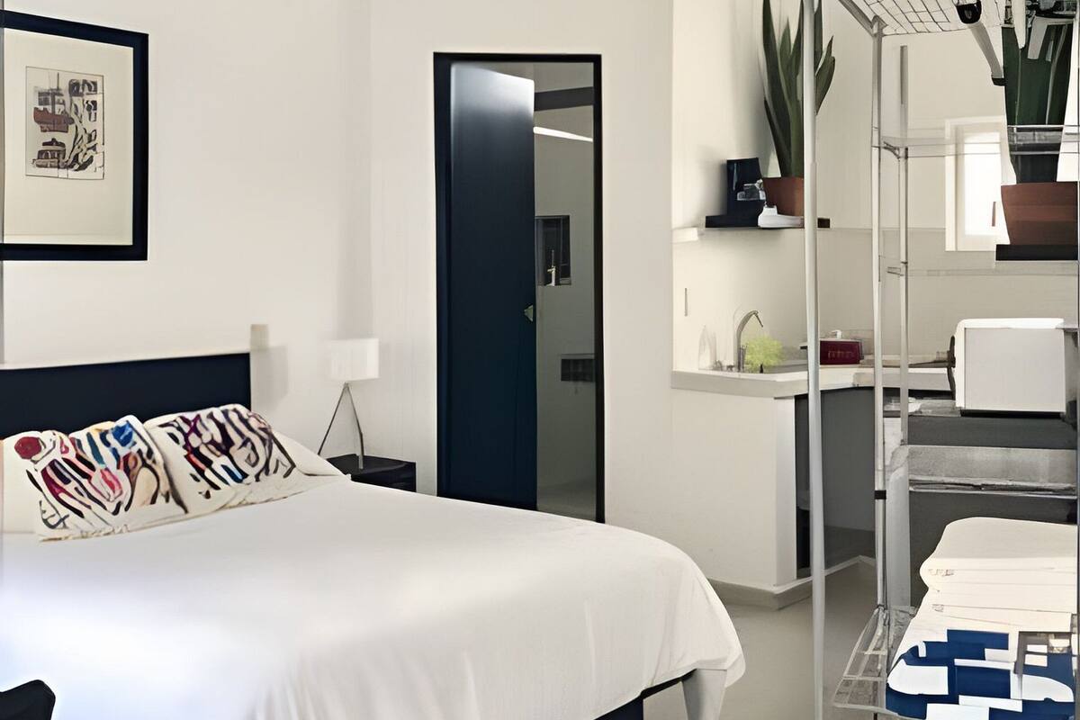 A modern bedroom with a bed, a ceiling fan, a desk with a chair, a mirror, and a shelving unit with plants.