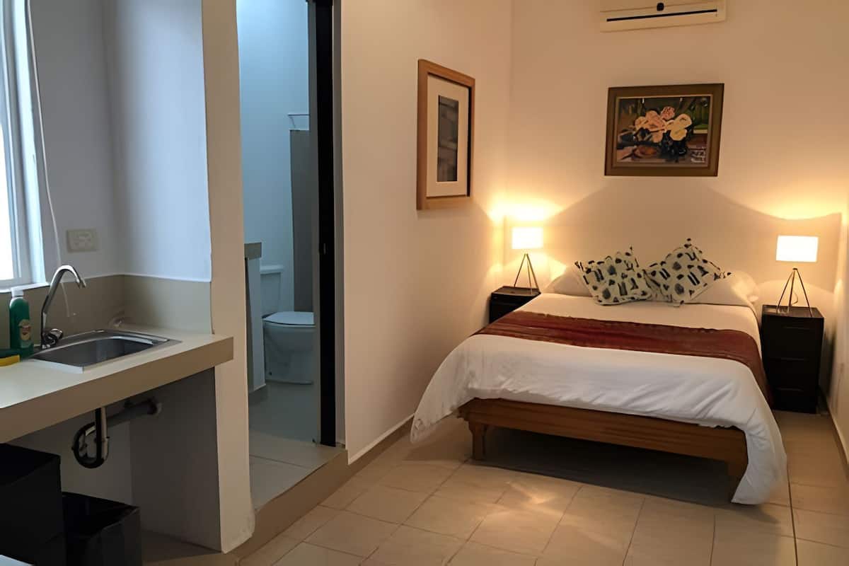 A bedroom with a bed, bedside lamps, a framed picture, and a bathroom visible through an open door.