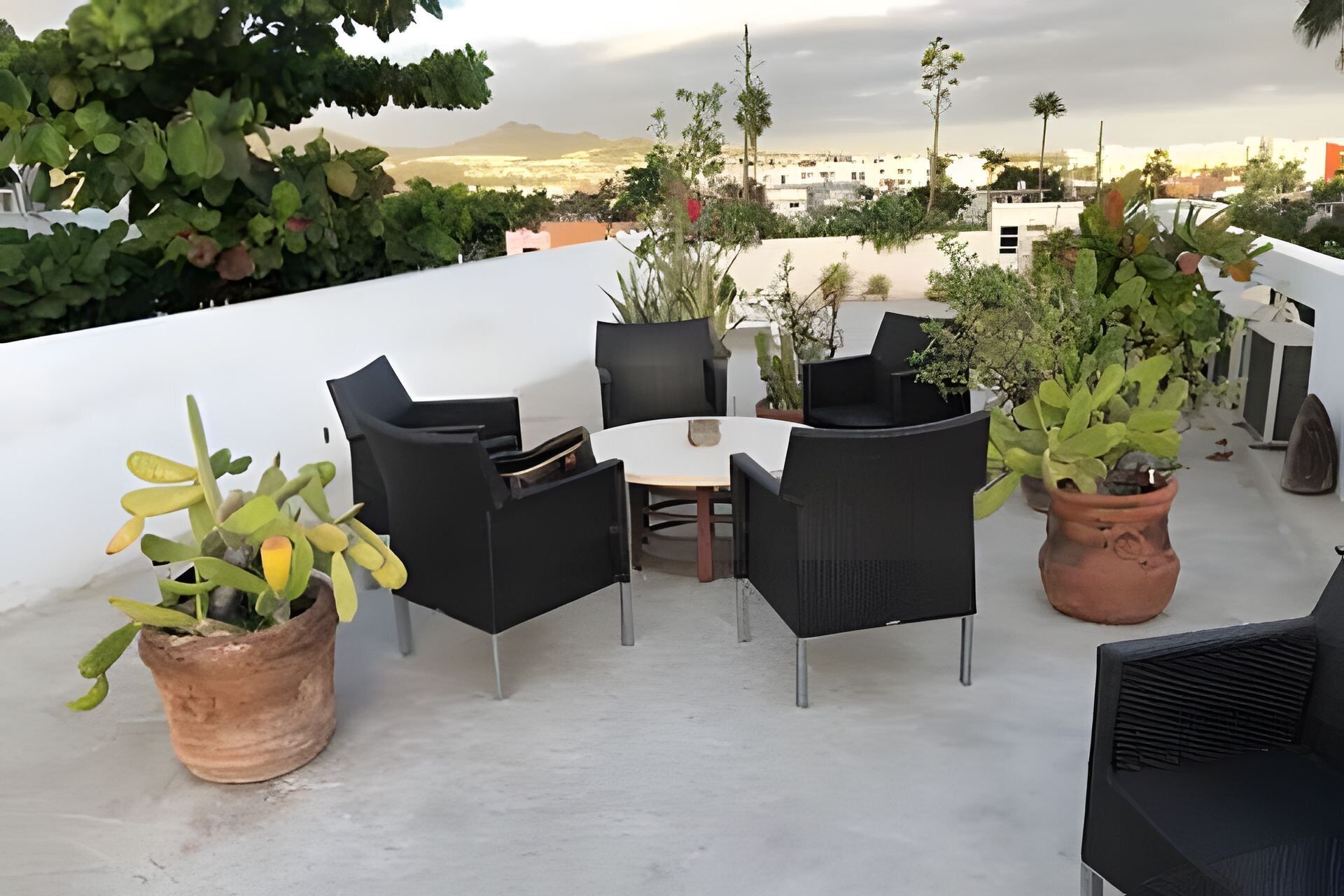 En tagterrasse med et rundt bord og fire stole, omgivet af krukker med planter.
