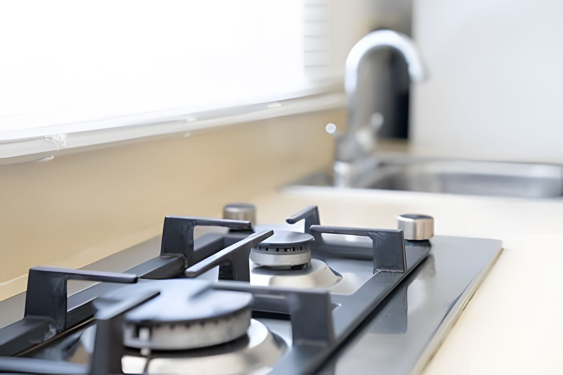 A kitchen with a gas stove, a faucet, and a window.