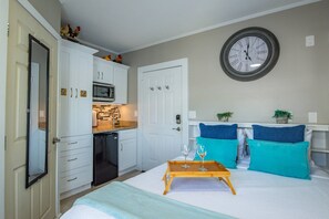 A bedroom with a bed, a bedside table with two wine glasses, a tray, and a clock on the wall. - Pierre's Perch: Discover Charm and Convenience, Perfect Studio Retreat in Key West with Shared Pool (Key West)