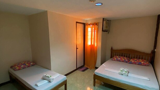 A small, clean room with two single beds, a wooden table, and a door leading to another room. - Princesa El Gallo Inn (Puerto Princesa)