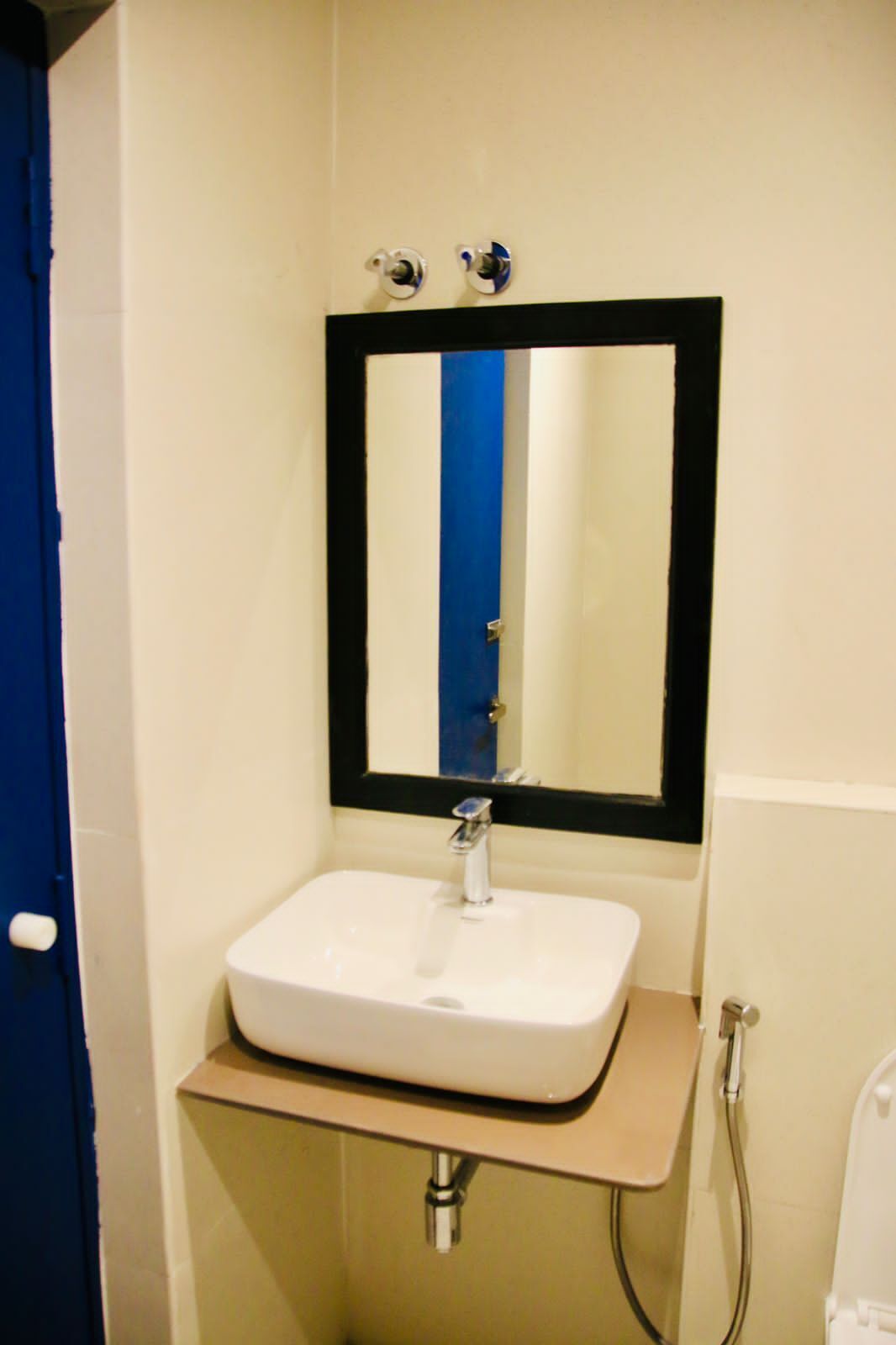 A bathroom with a white sink, a mirror with a black frame, and a blue door.