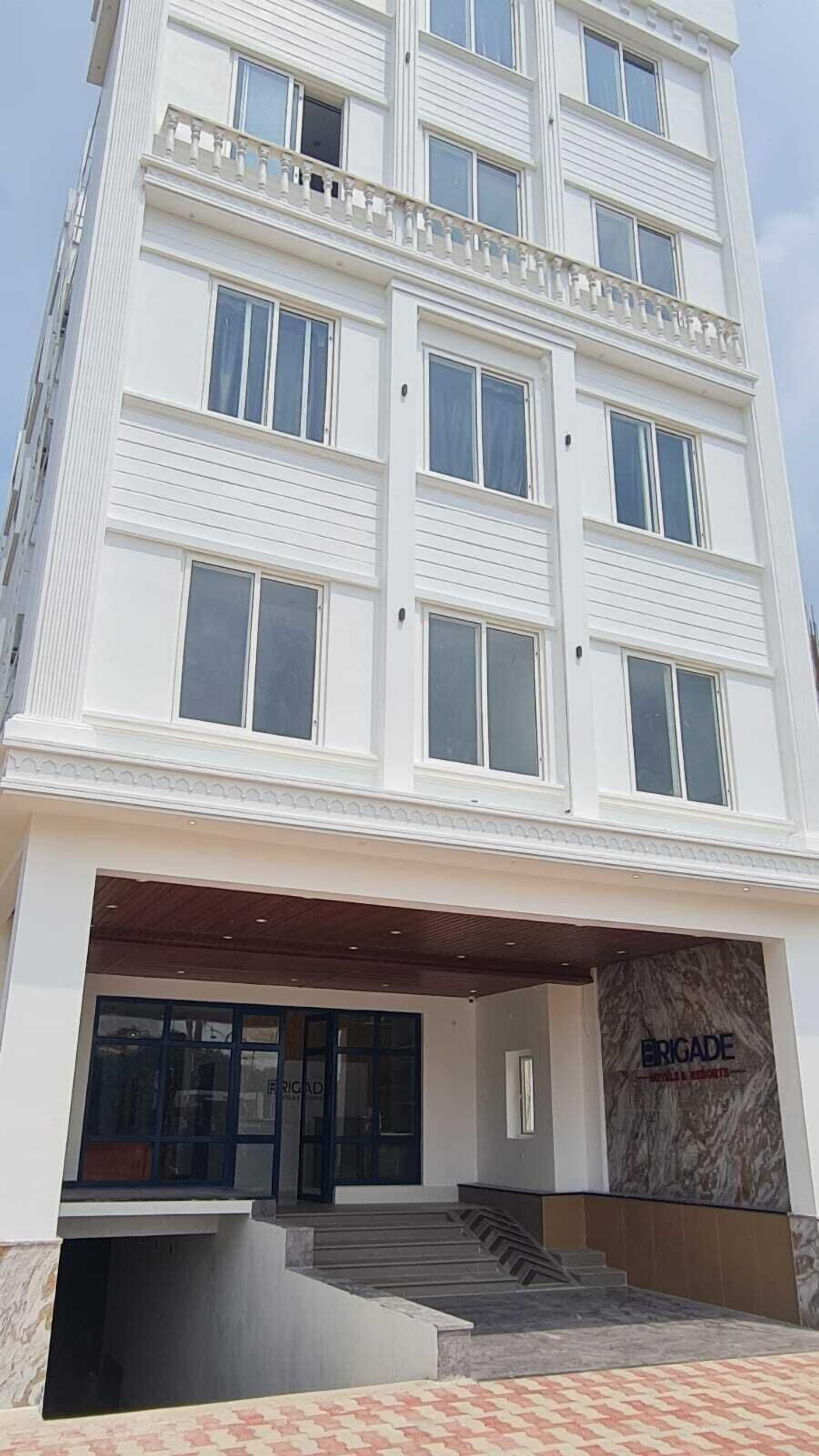 A multi-story hotel with a modern facade, large windows, and a prominent entrance with a marble wall and steps leading up to the door.