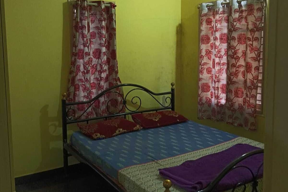 Un letto singolo con struttura in metallo, una ventola a soffitto e tende floreali.
