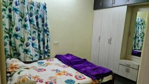 Une chambre à coucher avec un lit, des rideaux à motifs floraux, une couverture violette et une armoire.
