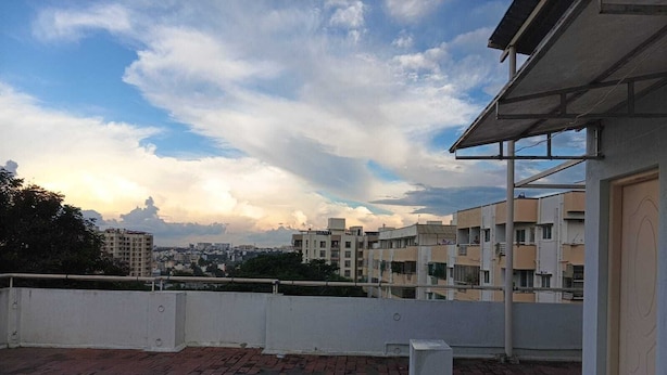 Une terrasse sur le toit, avec un sol en briques, une balustrade blanche et une vue sur les bâtiments environnants, sous un ciel partiellement nuageux.