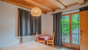 Een slaapkamer met een bed, een tafel, stoelen, een raam met gordijnen en uitzicht op groen.