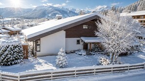 Een besneeuwde lodge met een houten gevel, een schuin dak en een uitzicht op besneeuwde bergen op de achtergrond.