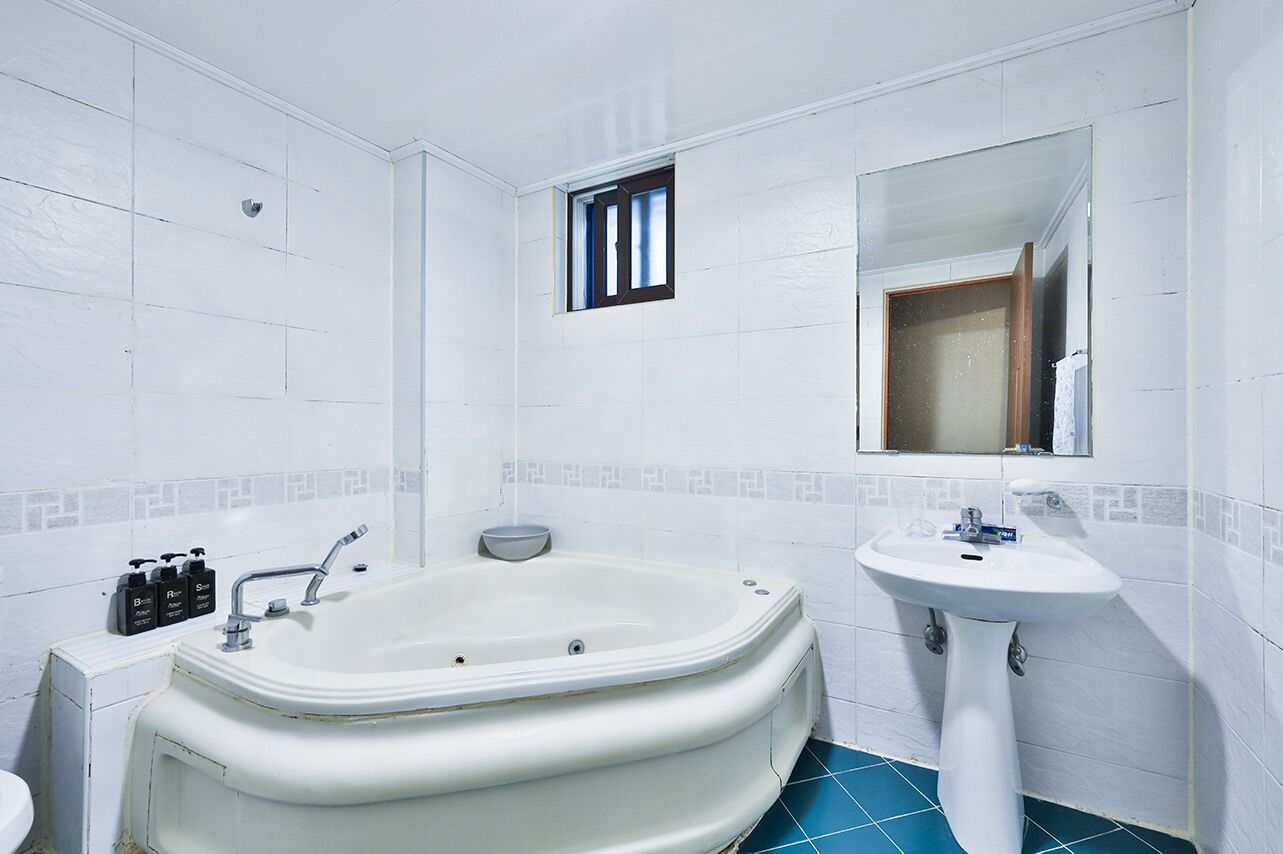 A bathroom with a bathtub, sink, and a window with blinds.