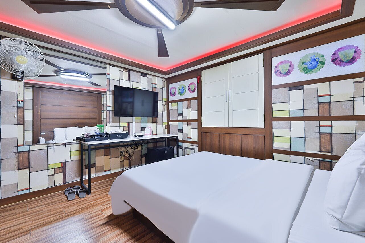 A hotel room with a bed, a desk with a computer, a TV, and a ceiling fan.