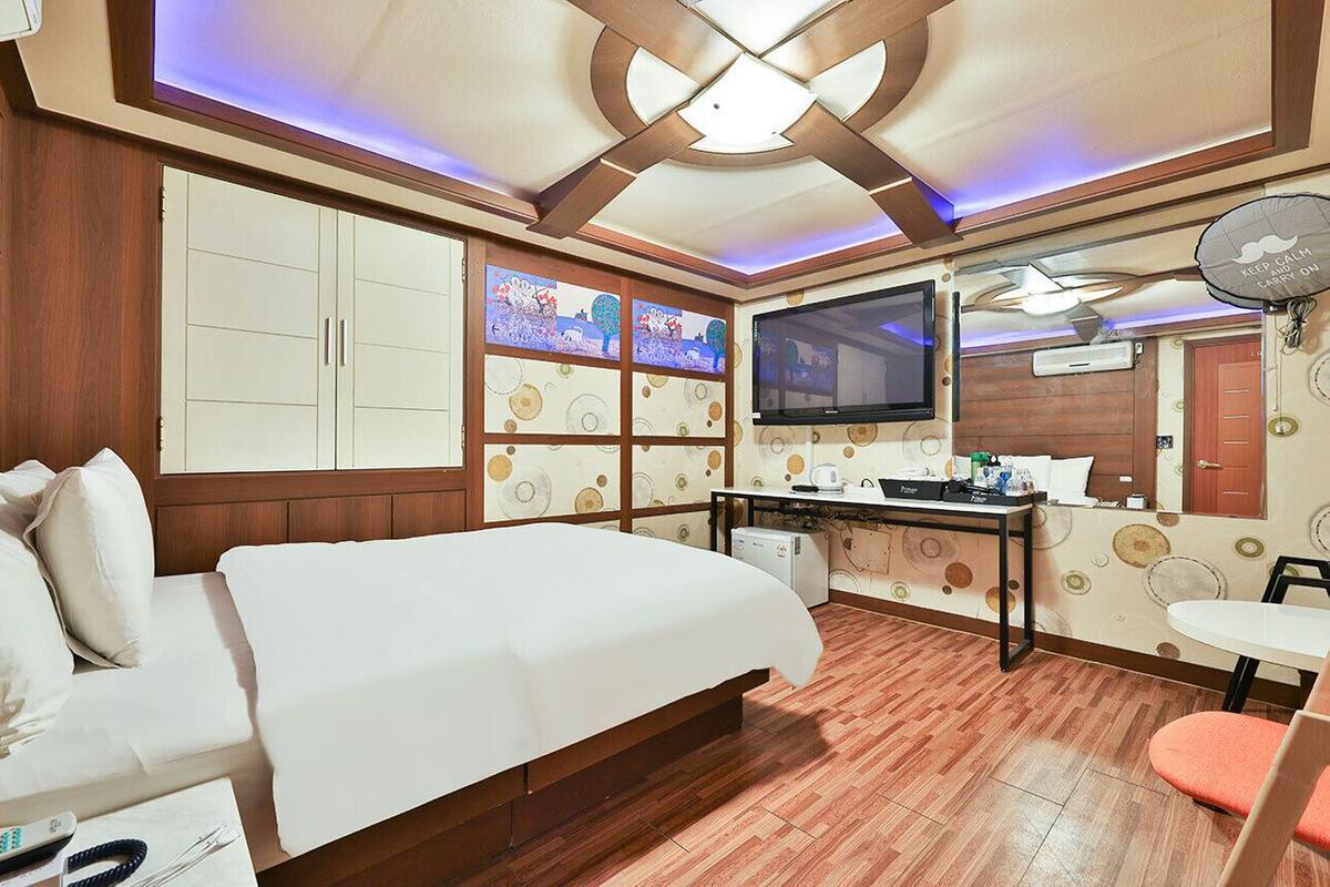 A hotel room with a bed, a desk with a computer, a TV, and a ceiling fan.