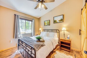 Quarto com cama, luminárias de cabeceira, mesa de cabeceira, ventilador de teto e duas pinturas na parede.