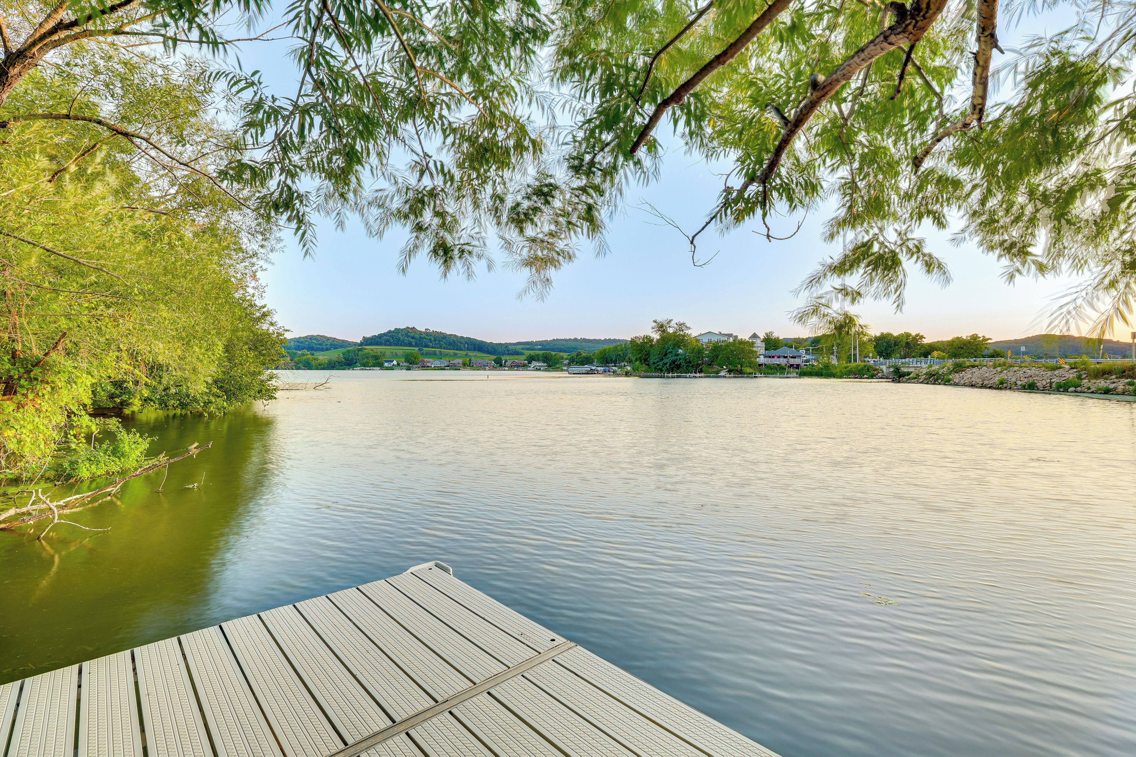 A wooden dock extending into calm water, surrounded by lush greenery and distant hills.
