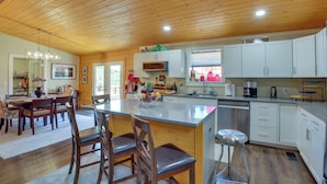 A spacious kitchen with wooden cabinets, a central island, and a dining area with chairs and a table. - Hot Springs Cabin w/ Deck + Mountain Views! (Hot Springs)