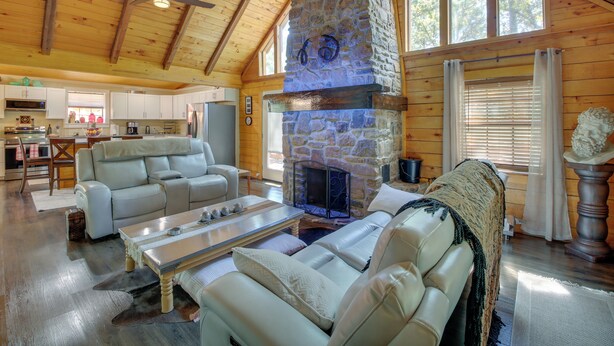 A spacious living area with a stone fireplace, wooden ceiling beams, and large windows. - Hot Springs Cabin w/ Deck + Mountain Views! (Hot Springs)