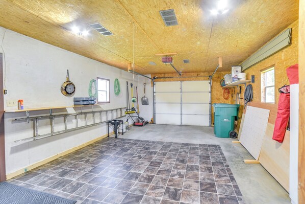 A garage with a tiled floor, a workbench, a power tool, and a green trash bin.