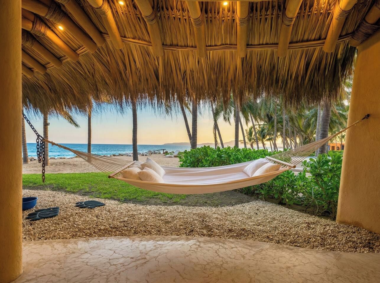 A hammock under a thatched roof, a pebble beach, and palm trees.