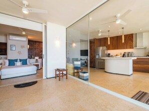 A modern hotel room with a large bed, a sitting area, and a kitchen area visible through a glass partition. - Mar de Coco Areca 101 (Playa Blanca)