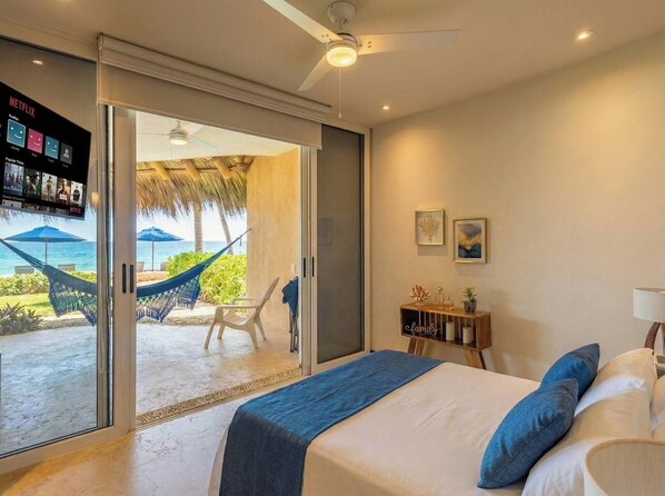 A bedroom with a bed, a TV, a desk, and a view of the ocean.