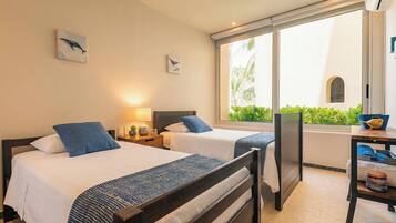 A hotel room with two beds, a desk, and a view of greenery outside.