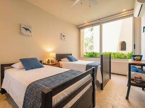 A hotel room with two beds, a desk, and a view of greenery outside.