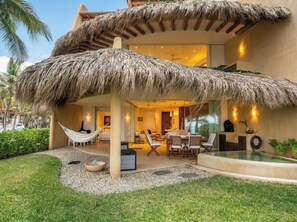 A modern outdoor lounge area with a thatched roof, seating, and a pool.